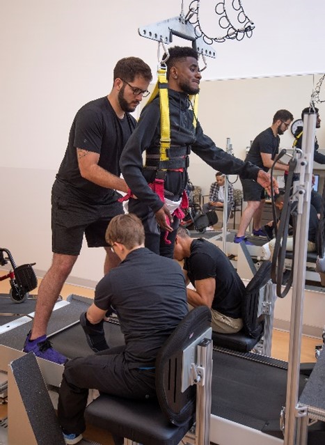 Patient in specialty harness on treadmill with care staff support.