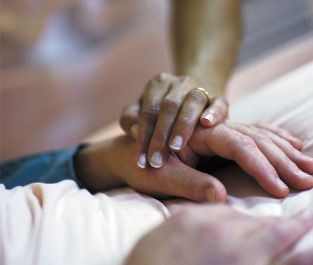Comforting hand on a patient's hand in a hospice bed.
