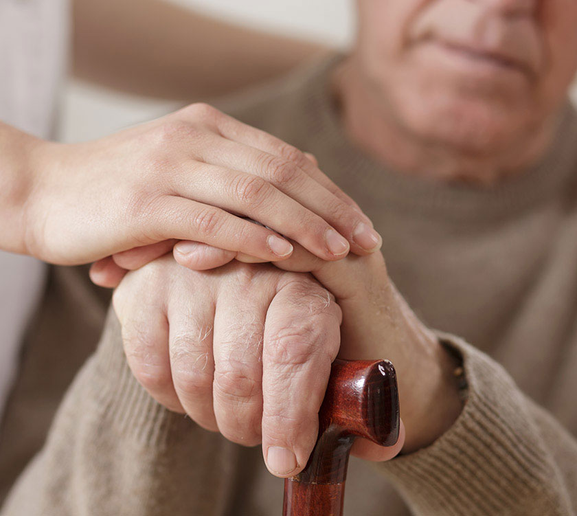 Health care provider holds the hand of a senior man who is holding a cane.