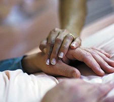 Comforting hand on a patient's hand in a hospice bed.