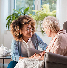 Young black woman kneels beside sitting senior.